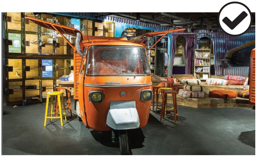 A rustic, colorful youth library with floor cushions and a small orange vehicle that has been converted into bar seating.